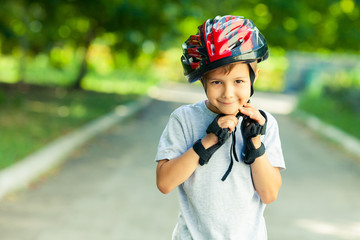 Little boy riding on rollers in the summer in the Park. Happy child in helmet learning to skate.