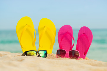 Fototapeta na wymiar Glasses with yellow and pink sandals stand in the sand against the background of the sea