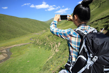 Fototapeta premium young woman hiker taking photo with smart phone in mountains