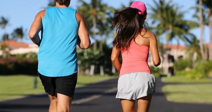 Couple running and jogging in rich beautiful residential neighborhood on summer day. Fit woman and man recreational runners exercising together running away from camera.