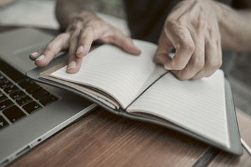 Close-up. The young man opened a notebook on the table. there is a laptop near by