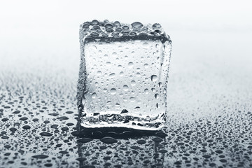Transparent ice cube on glass with water drops