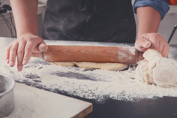 Baking concept. Hands roll dough on black background.