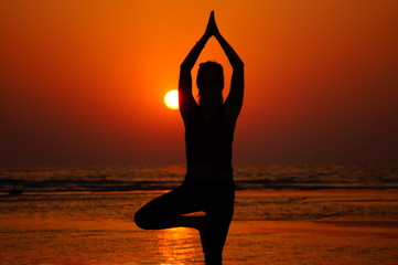 Yoga on the sunset, silhouette of the girl on the sea, yoga pose