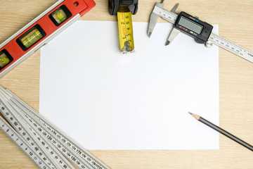 Top view of ruler, water level, vernier caliper, pencil and measure tape on blank paper background.