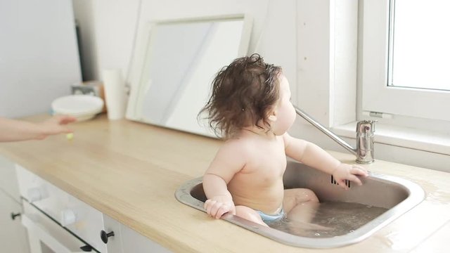 Baby taking bath in kitchen sink. sunny bathroom with window. Little girl bathing. Water fun for kids. Hygiene and skin care for children. Bath room interior