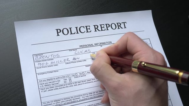 Filing a police report by hand at a desk. This form is randomly filled with no real names or numbers.