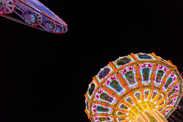 Ferris Wheel and a Swing Carousel against black background at night.