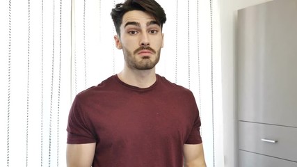 Cool handsome young man shrugging and being unsure, at home in his living-room looking at camera - Powered by Adobe