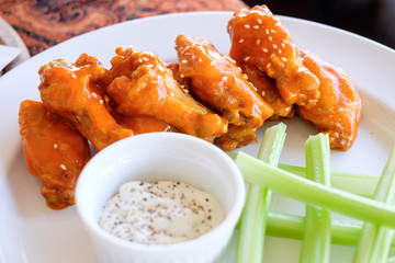 Buffalo wings / barbecue chicken wings on white dish with celery and white dip sauce as side dish for pizza. Closeup view.