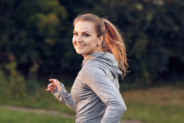Cheerful sporty woman running at park in sunrise