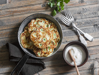Potato, leek and green pea pancakes in the pan on wooden background, top view. Simple rustic food