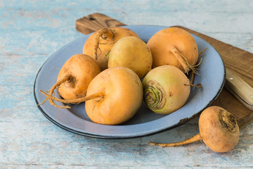  Vegetables.  Fresh raw turnip in a blue round bowl, next to a cutting board and a knife on an old wooden table.