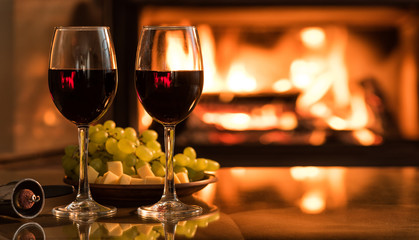 Two red wine wineglasses over fireplace background.