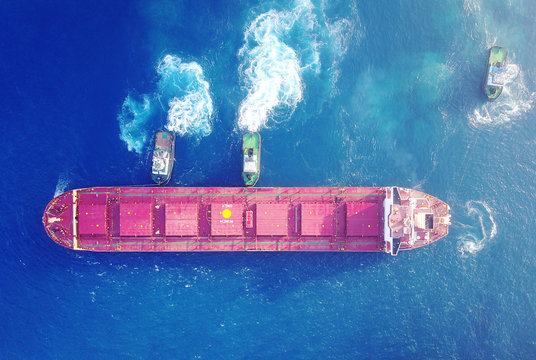 Large bulk carrier ship pulled by tow-three  tugboats in the port 