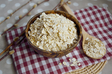 Raw oat flakes in a wooden bowl with a spoon on the table, healthy food
