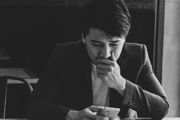 Desperate sad young businessman looking at bad text message on his mobile phone. Black and white tone