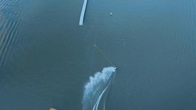 OVERHEAD aerial drone shot of female wake boarding in a cable wakepark on a lake. 4K UHD 60 FPS 