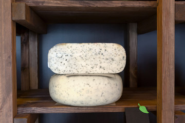 Hard cheese with herbs in wheel and piece on grocery shop shelf