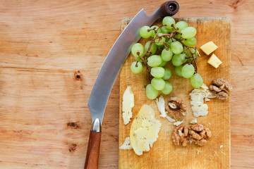 Cheese platter, sliced cheese on natural wood board with grapes and nuts
