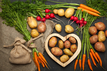 Carrots, radishes and potatoes on a black wooden background