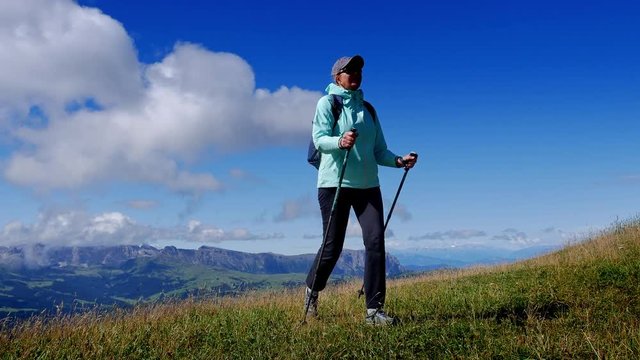 Hiker climbs the green slope agains a backdrop of mountains and blue sky