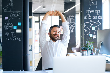 Businessman at the desk in his office stretching arms.