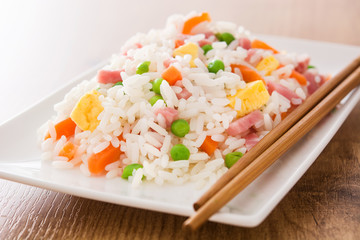 Chinese fried rice with vegetables and omelette on wooden table
