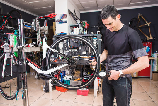 Male involved master is measuring a pressure in tyres of the bicycle in a special workshop