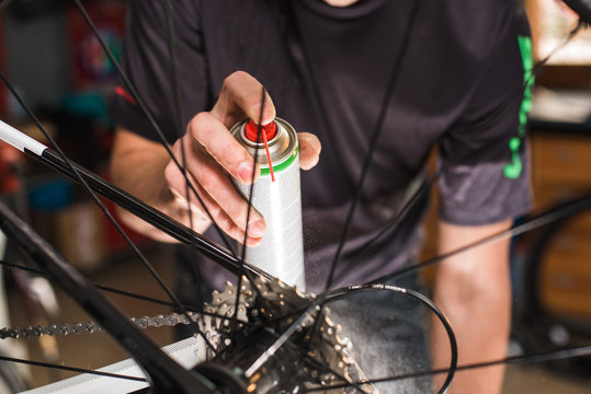 Male hands cleaning and oiling a bicycle chain and gear with oil spray