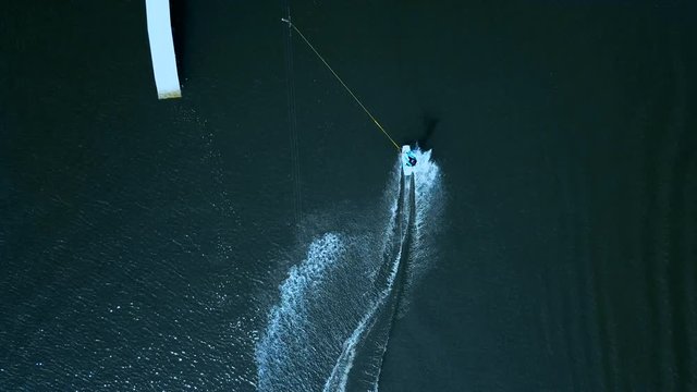 OVERHEAD aerial drone shot of female wake boarding in a cable wakepark on a lake. 4K UHD 60 FPS 