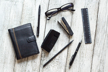 Black and white still life: opened blank notepad, notebooks, pen, pencil, glasses, purse.
