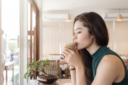 Young happy Asian woman drinking coffee in the coffee shop.