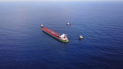 Large bulk carrier ship pulled by tugboats in open water