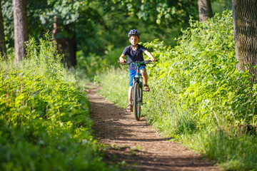 Naklejka premium Small boy in protective helmet riding bicycle in park on summer day