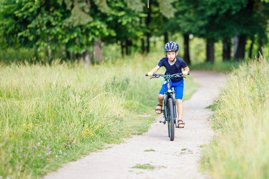 Small boy in protective helmet riding bicycle in park on summer day