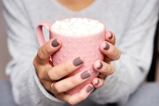 female hands holding pink cup of coffee with marshmallow