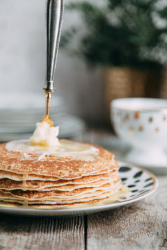 pancakes with butter and sour cream on light wooden background composition with flowers and tea