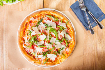 Top view Pizza with prosciutto, parma ham, arugula and parmesan on served wooden restaurant table. Italian cuisine. Selective focus, copy space