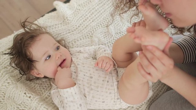 Mother kisses baby daughter feet while playing on a white bed