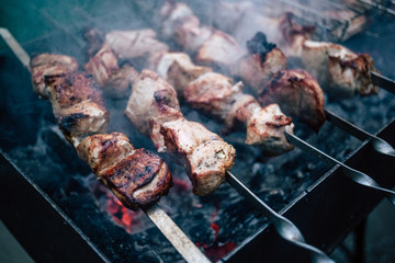 Grilled kebab cooking on metal skewers (grill). Roasted meat cooked at barbecue with smoke. Close up BBQ fresh pork meat chop slices. Traditional eastern dish, shish kebab.