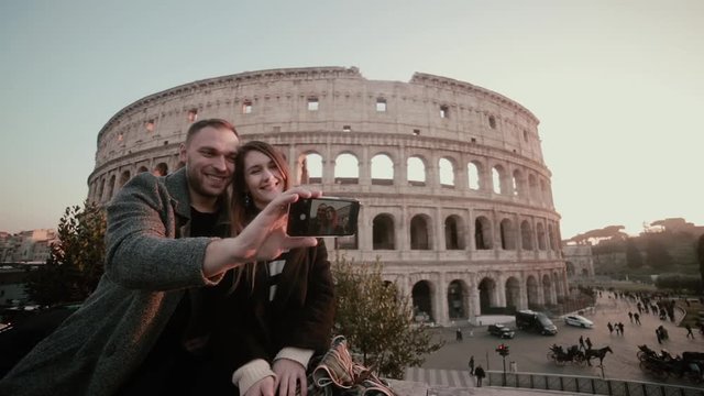 Young happy couple taking a selfie photo on smartphone. Attractive man and woman near the Colosseum in Rome, Italy.