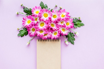 Floral mockup. Notebook near pink flowers on purple background top view