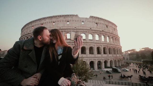 Happy young couple taking a selfie photo near the Colosseum in Rome, Italy. Handsome man kisses woman, smiling.