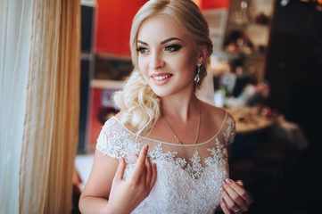 Fototapeta premium Beautiful young blonde bride in a beautiful dress with lace at home preparing for the wedding. Waiting for the groom.