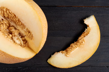 Fresh sweet yellow melon sliced on wooden black background. Piece of raw organic melon isolated on wooden dark surface close up. Top view