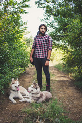 Naklejka na ściany i meble Handsome bearded man with guitar bag and husky dog walking in the woods at summer times 