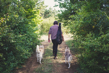 Handsome bearded man with guitar bag and husky dog walking in the woods at summer times  