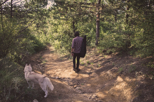 Handsome Bearded Man With Guitar Bag And Husky Dog Walking In The Woods At Summer Times  