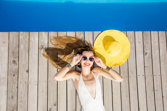 Playful woman lying with yellow sunhat on the poolside. Summer vacation concept